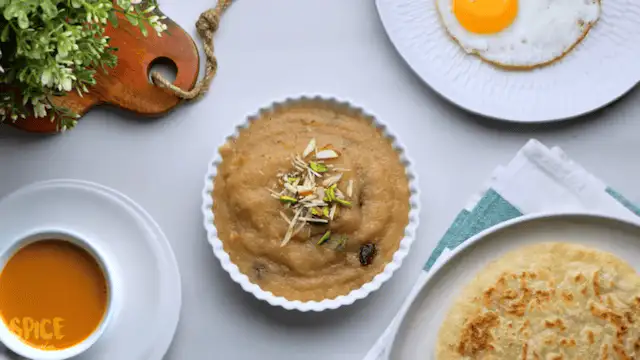 Semolina Halwa/suji halwa in a serving bowl with paratha, egg, and caramel pudding