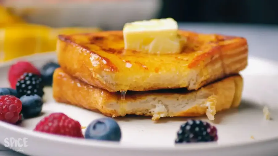 Classic French Toast For Breakfast on a serving plate with some berries, butter, and honey