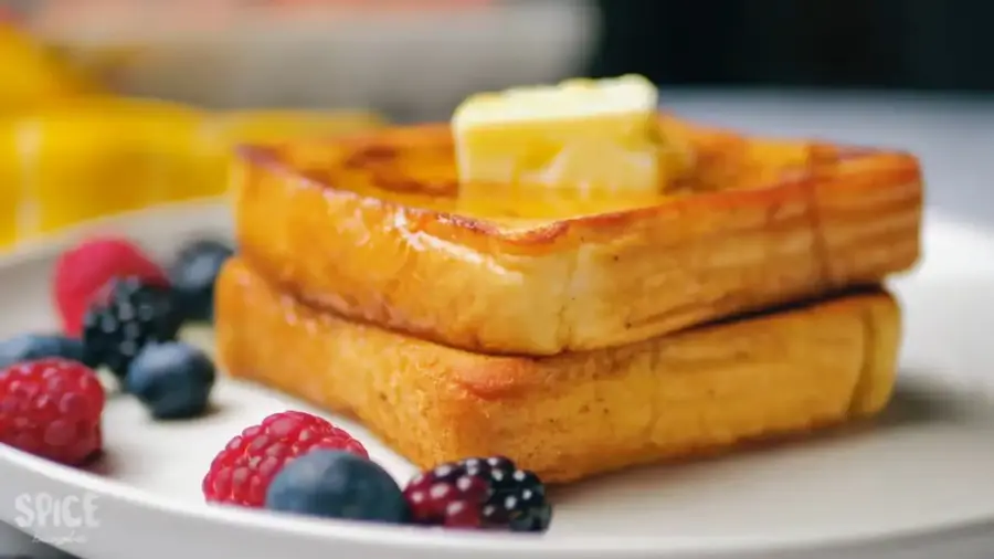 Classic French Toast For Breakfast on a serving plate with some berries, butter, and honey