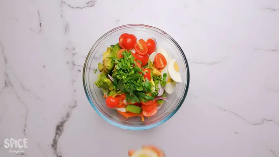 egg salad recipe with tomato, cucumber, eggs, and avocado in a large mixing bowl