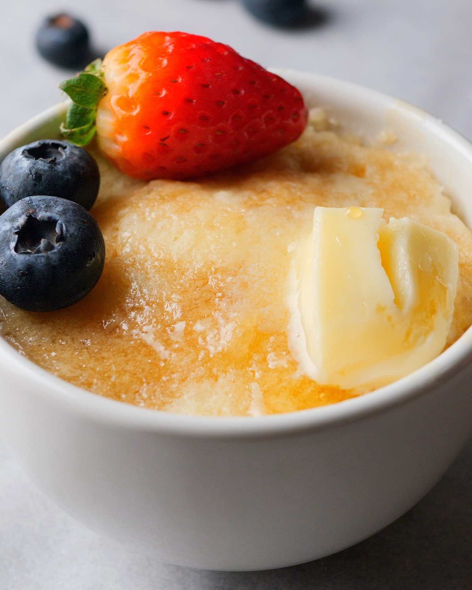 a picture of a pancake made in a mug topped with blueberry and strawberry