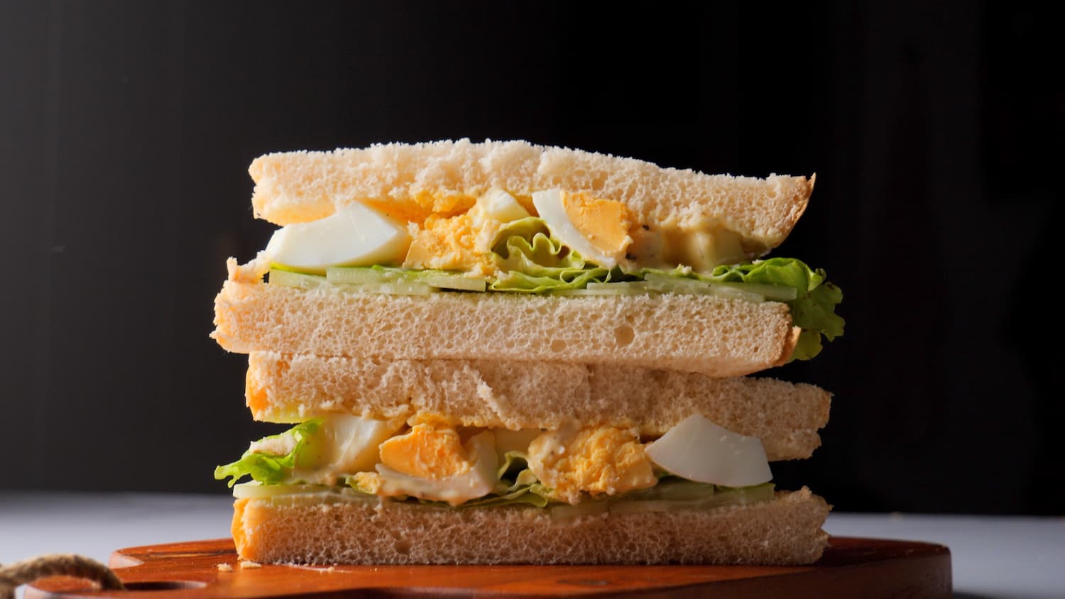 stakes of egg salad sandwich on a chopping board