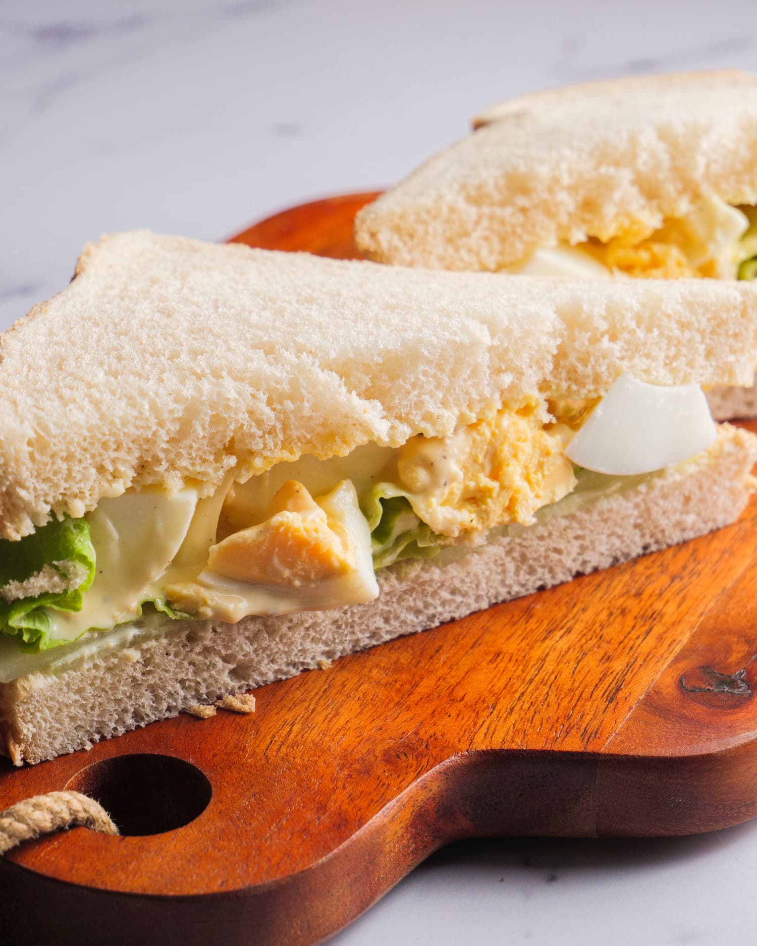 stakes of egg salad sandwich on a chopping board