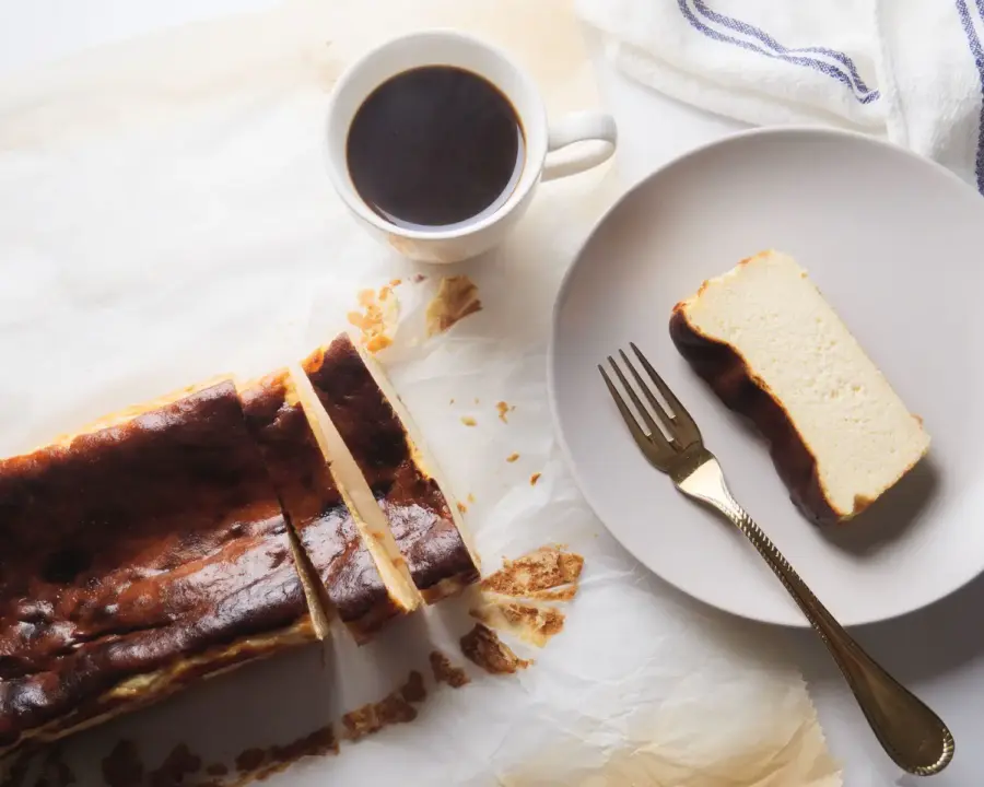 Loaf Pan Basque Cheesecake on a serving board with a slice, fork, and coffee