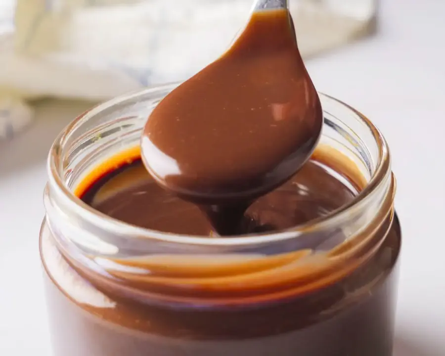 Hot Fudge Sauce recipe into a jar with a spoon
