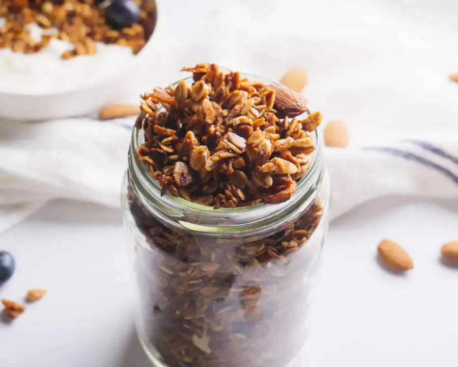 Vanilla Almond Granola into a jar on a kitchen counter