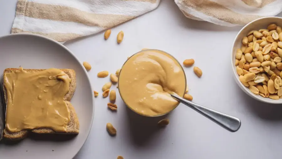 Honey Roasted Peanut Butter in a glass jar with a spoon, bread with peanut butter